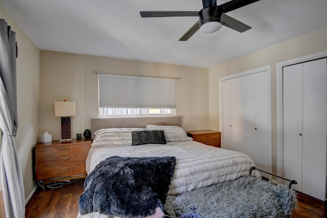 bedroom with dark wood finished floors, a ceiling fan, and two closets