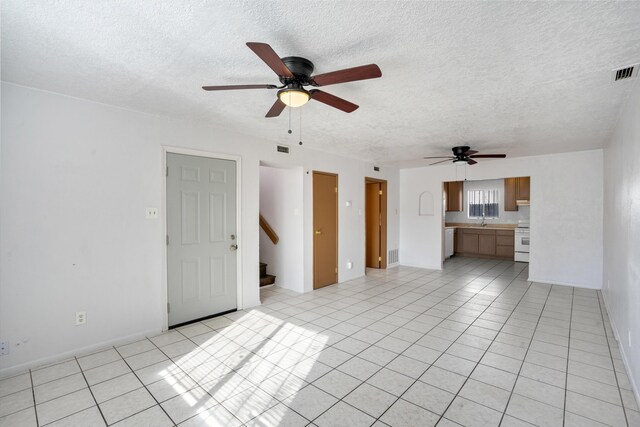 unfurnished living room featuring ceiling fan, light tile patterned floors, and a textured ceiling