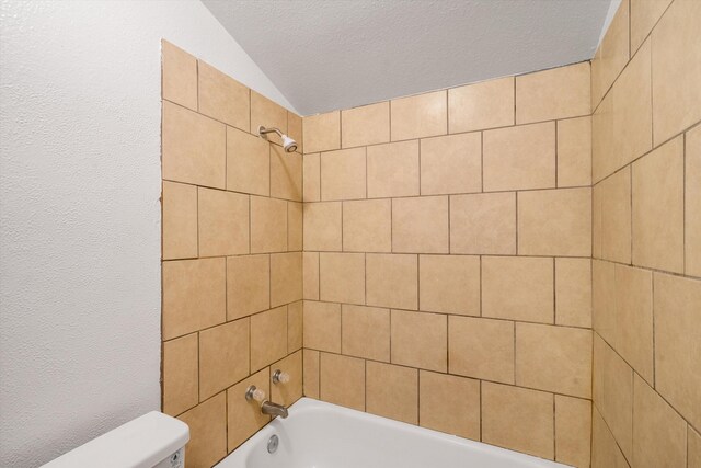 bathroom with vaulted ceiling, tiled shower / bath, a textured ceiling, and toilet