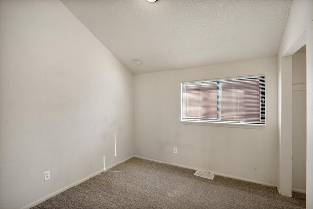 carpeted empty room featuring a textured ceiling and vaulted ceiling