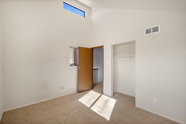 unfurnished bedroom with light colored carpet, high vaulted ceiling, and a closet