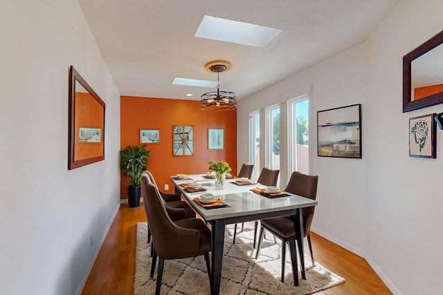 dining space with a skylight, light hardwood / wood-style floors, and a notable chandelier