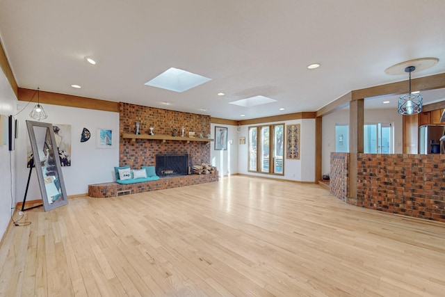 unfurnished living room with a skylight, light hardwood / wood-style flooring, and a brick fireplace