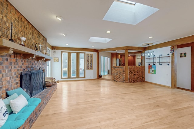 unfurnished living room with a skylight, a fireplace, brick wall, and light wood-type flooring