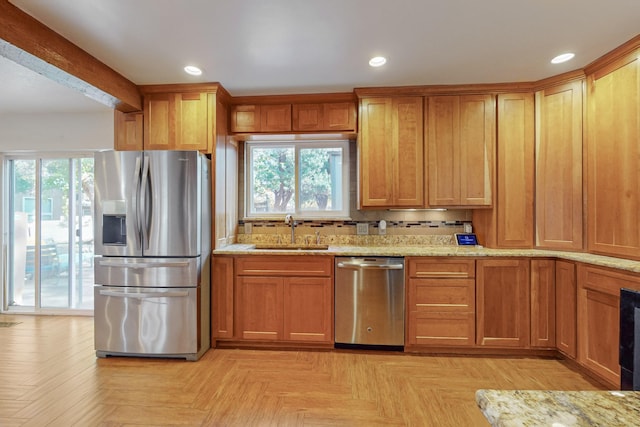 kitchen with sink, light stone countertops, stainless steel appliances, and light parquet flooring