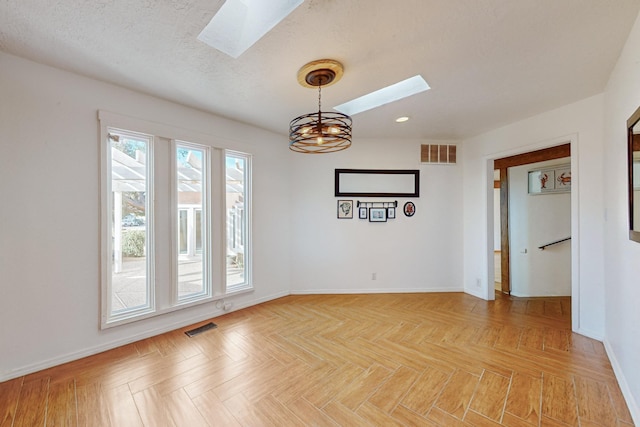 empty room featuring a chandelier, a textured ceiling, light parquet flooring, and a skylight