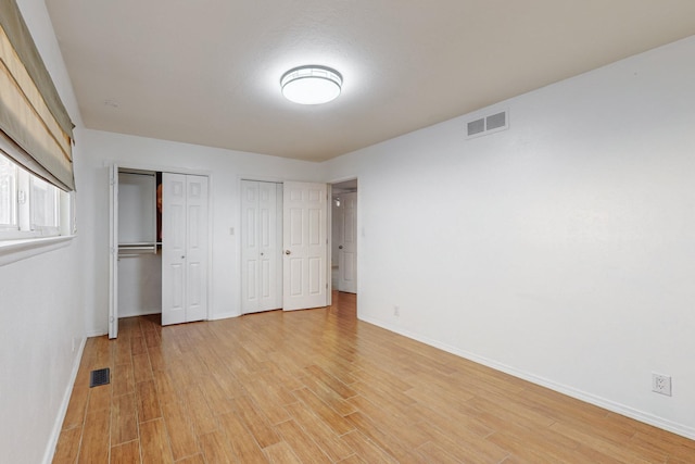 unfurnished bedroom with multiple closets and light hardwood / wood-style flooring