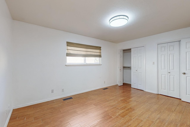 unfurnished bedroom featuring multiple closets and light hardwood / wood-style floors