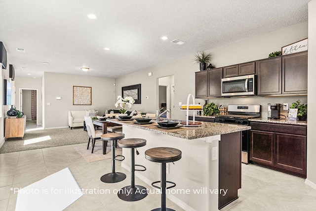 kitchen featuring a kitchen bar, a textured ceiling, dark brown cabinetry, stainless steel appliances, and an island with sink