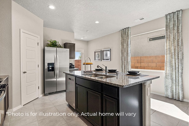 kitchen with light stone countertops, sink, stainless steel appliances, a textured ceiling, and a kitchen island with sink