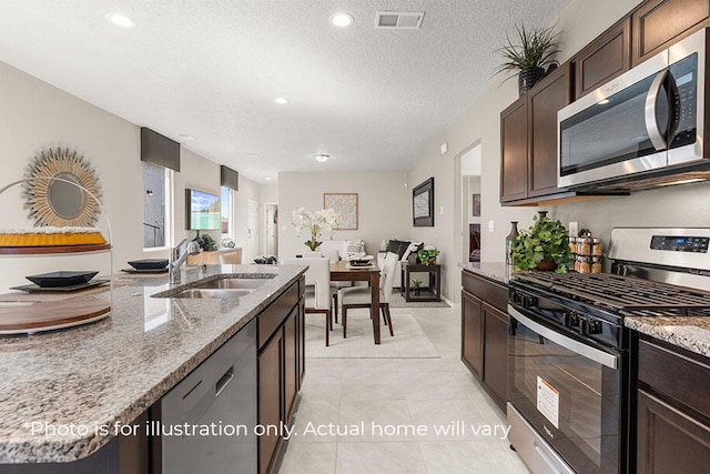 kitchen with sink, light stone countertops, a textured ceiling, light tile patterned floors, and stainless steel appliances