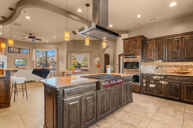 kitchen with light stone countertops, a center island, ceiling fan, hanging light fixtures, and island exhaust hood