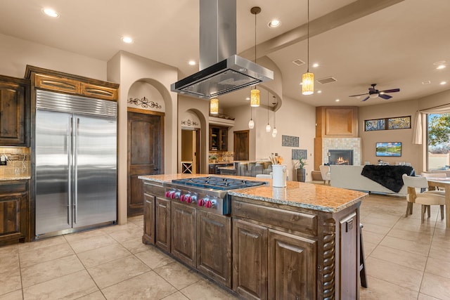 kitchen featuring pendant lighting, a center island, a tiled fireplace, island exhaust hood, and stainless steel appliances