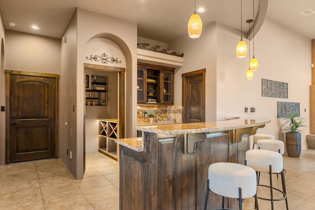 bar with tasteful backsplash, light stone counters, dark brown cabinetry, light tile patterned floors, and decorative light fixtures