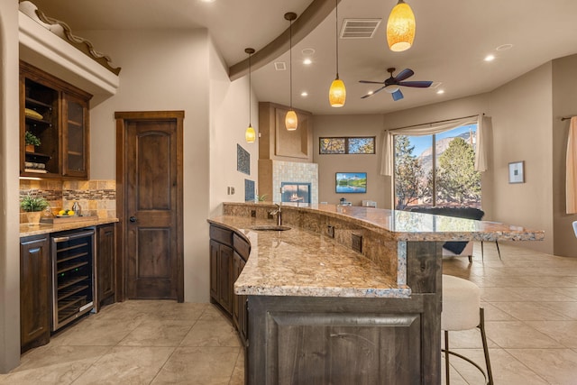 kitchen with pendant lighting, sink, wine cooler, a kitchen bar, and kitchen peninsula