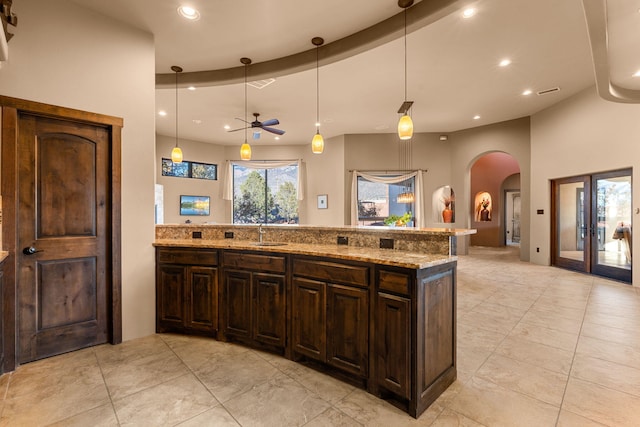 kitchen with pendant lighting, sink, ceiling fan, dark brown cabinets, and light stone counters