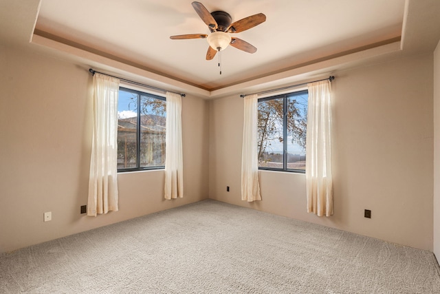 carpeted spare room with a tray ceiling and ceiling fan