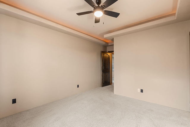 empty room with a tray ceiling, ceiling fan, and carpet