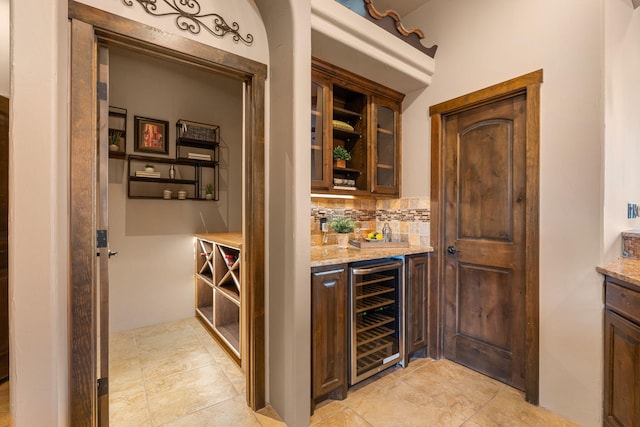 bar featuring dark brown cabinets, tasteful backsplash, wine cooler, and light stone counters