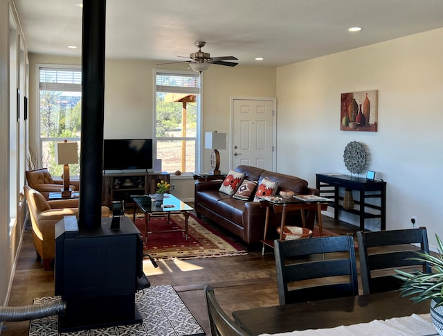 living room featuring ceiling fan, dark hardwood / wood-style floors, a wood stove, and a wealth of natural light