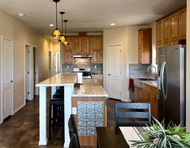 kitchen featuring sink, stainless steel appliances, light stone counters, decorative light fixtures, and a kitchen island