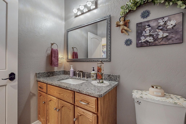 bathroom with a textured wall, vanity, and toilet