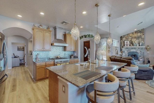 kitchen featuring arched walkways, wall chimney exhaust hood, open floor plan, light stone countertops, and a sink