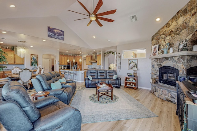 living area featuring visible vents, arched walkways, a ceiling fan, light wood-style flooring, and a stone fireplace