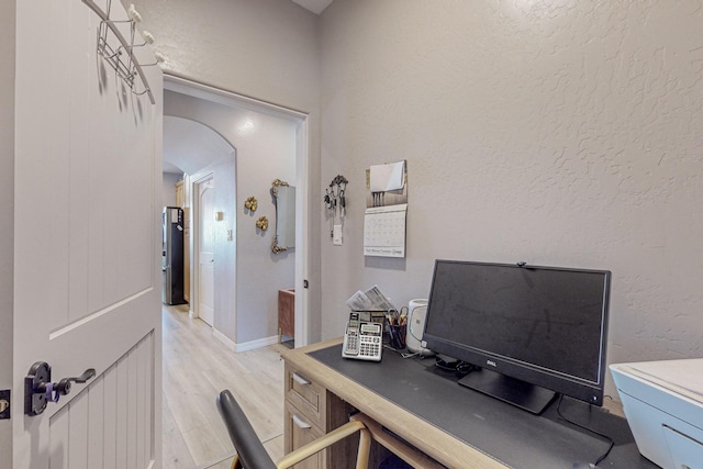 office space with light wood-style flooring, arched walkways, baseboards, and a textured wall