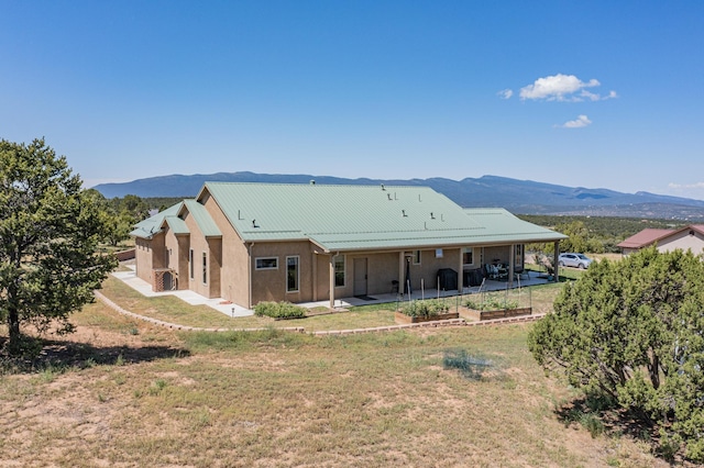 back of house featuring metal roof, a yard, a patio area, a mountain view, and stucco siding