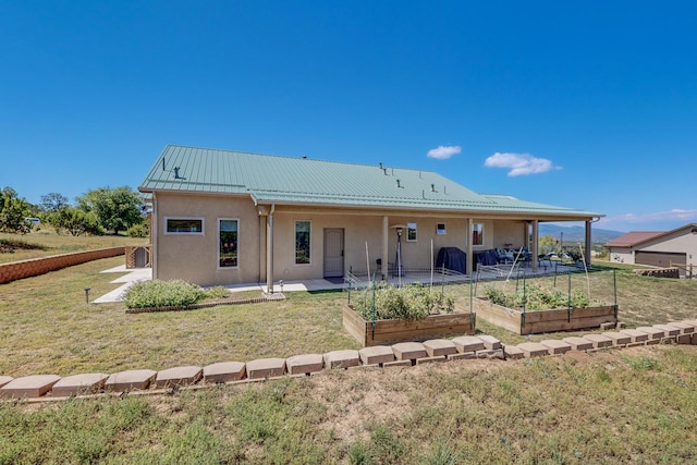 back of house with a vegetable garden, a lawn, metal roof, a patio area, and stucco siding