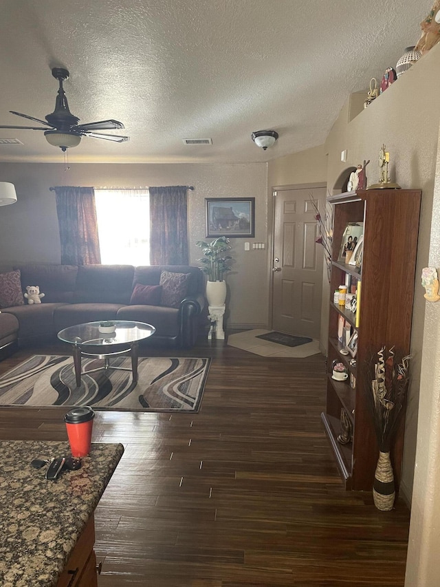 living room featuring dark wood-style floors, ceiling fan, a textured ceiling, and visible vents