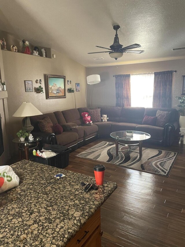 living room with a textured ceiling, ceiling fan, and dark wood-type flooring