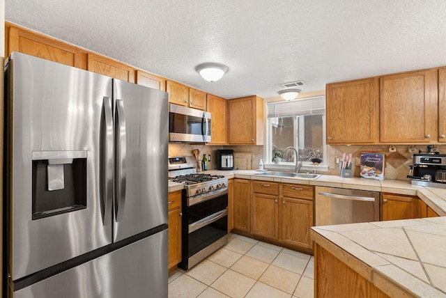 kitchen featuring tile countertops, sink, light tile patterned floors, a textured ceiling, and stainless steel appliances