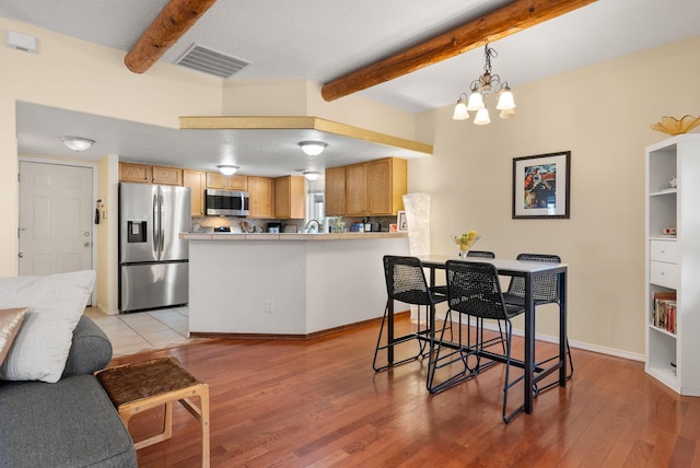 kitchen with beam ceiling, stainless steel appliances, a notable chandelier, kitchen peninsula, and light wood-type flooring