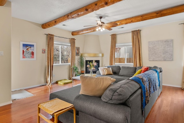 living room featuring a fireplace, beam ceiling, light wood-type flooring, and ceiling fan