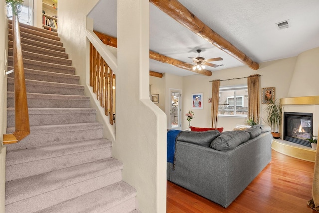 living room with a fireplace, wood-type flooring, ceiling fan, and beam ceiling