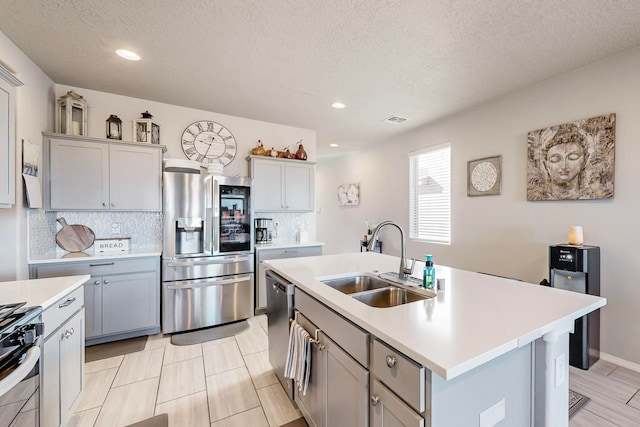 kitchen with sink, backsplash, a textured ceiling, a kitchen island with sink, and appliances with stainless steel finishes