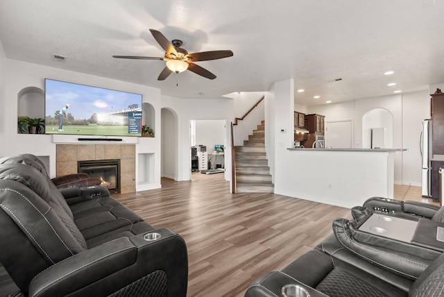 living room with a tiled fireplace, ceiling fan, hardwood / wood-style floors, and a textured ceiling