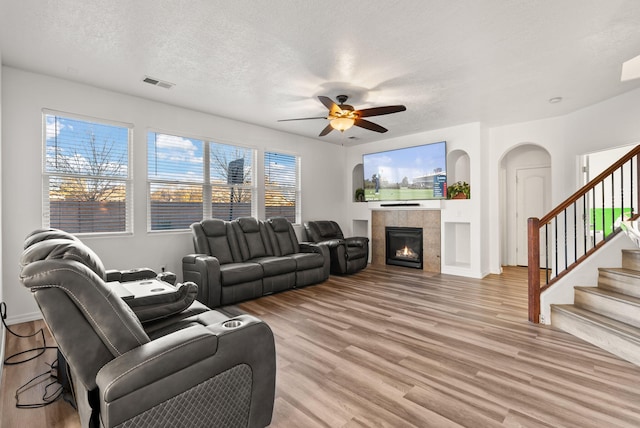 living room with ceiling fan, a tiled fireplace, a textured ceiling, and light hardwood / wood-style flooring