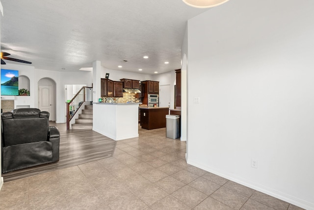 kitchen with ceiling fan, a textured ceiling, tasteful backsplash, a kitchen island, and dark brown cabinetry