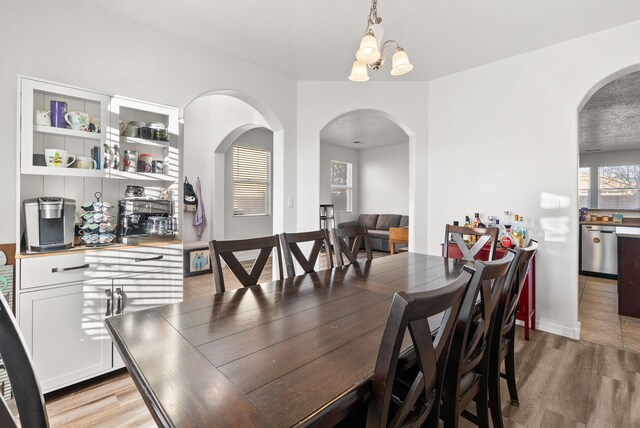 6923 Wrangell Loop NE, Rio Rancho, NM 87144 - dining space with arched walkways, light wood finished floors, a chandelier, and baseboards