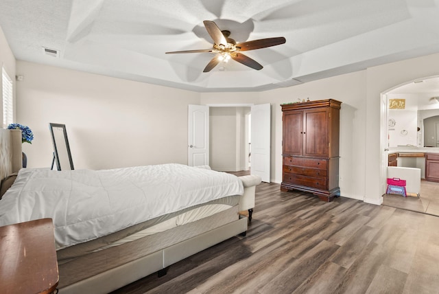 bedroom featuring ensuite bath, ceiling fan, dark hardwood / wood-style floors, a textured ceiling, and a tray ceiling