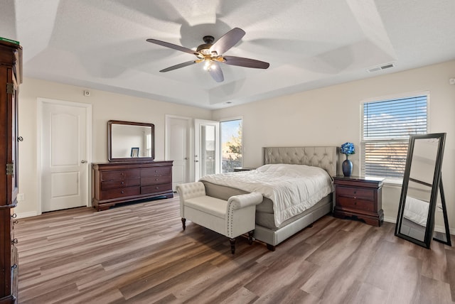 bedroom featuring a tray ceiling, ceiling fan, a textured ceiling, and hardwood / wood-style flooring