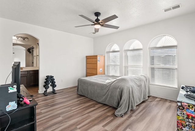 bedroom with ensuite bath, ceiling fan, hardwood / wood-style floors, and a textured ceiling