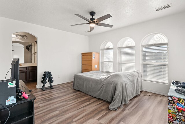 6923 Wrangell Loop NE, Rio Rancho, NM 87144 - bedroom featuring light wood finished floors, arched walkways, ensuite bathroom, a textured ceiling, and ceiling fan