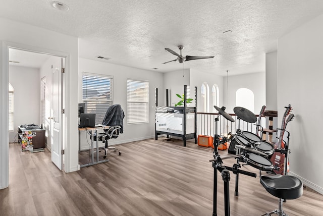 workout area with a textured ceiling, light wood-type flooring, and ceiling fan