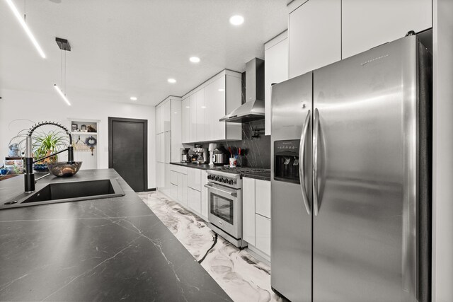 kitchen with appliances with stainless steel finishes, tasteful backsplash, wall chimney exhaust hood, sink, and white cabinetry