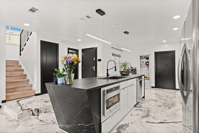 kitchen featuring sink, stainless steel appliances, pendant lighting, a textured ceiling, and a center island with sink