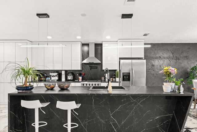 kitchen featuring white cabinets, wall chimney exhaust hood, stainless steel fridge with ice dispenser, and hanging light fixtures